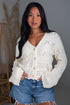 Woman wearing a white lace cardigan and denim shorts indoors.