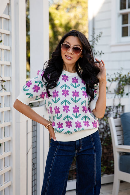 Woman wearing a colorful floral-patterned sweater and sunglasses outdoors.