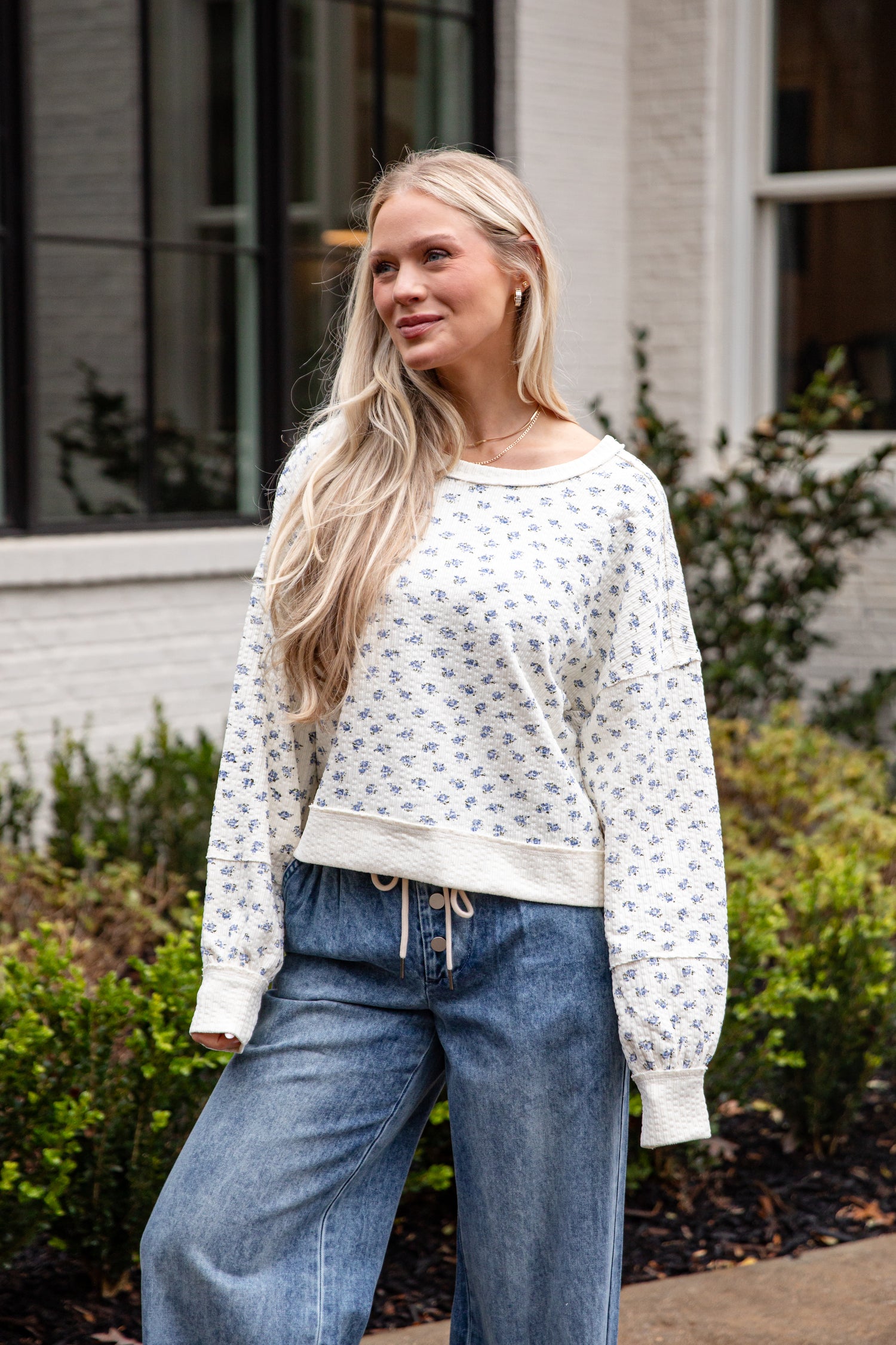 Woman wearing a white patterned sweater and blue jeans standing outdoors.