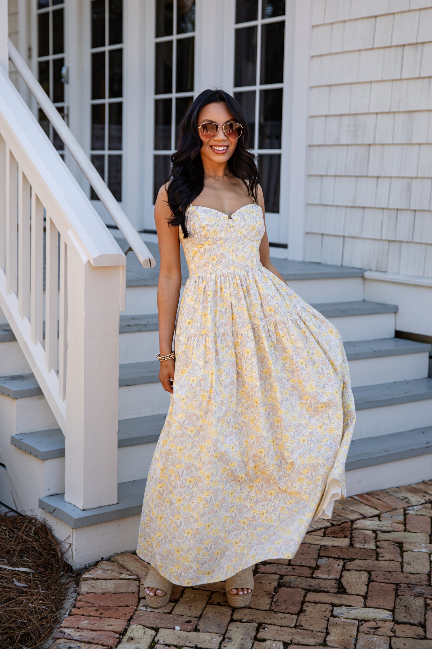 Woman in a yellow floral dress standing on a staircase outside a house.