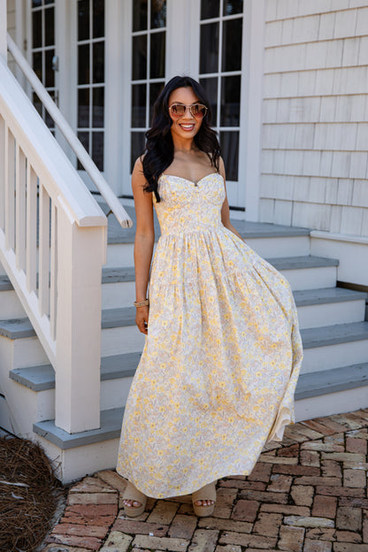 Woman in a yellow floral dress standing on a staircase outside a house.