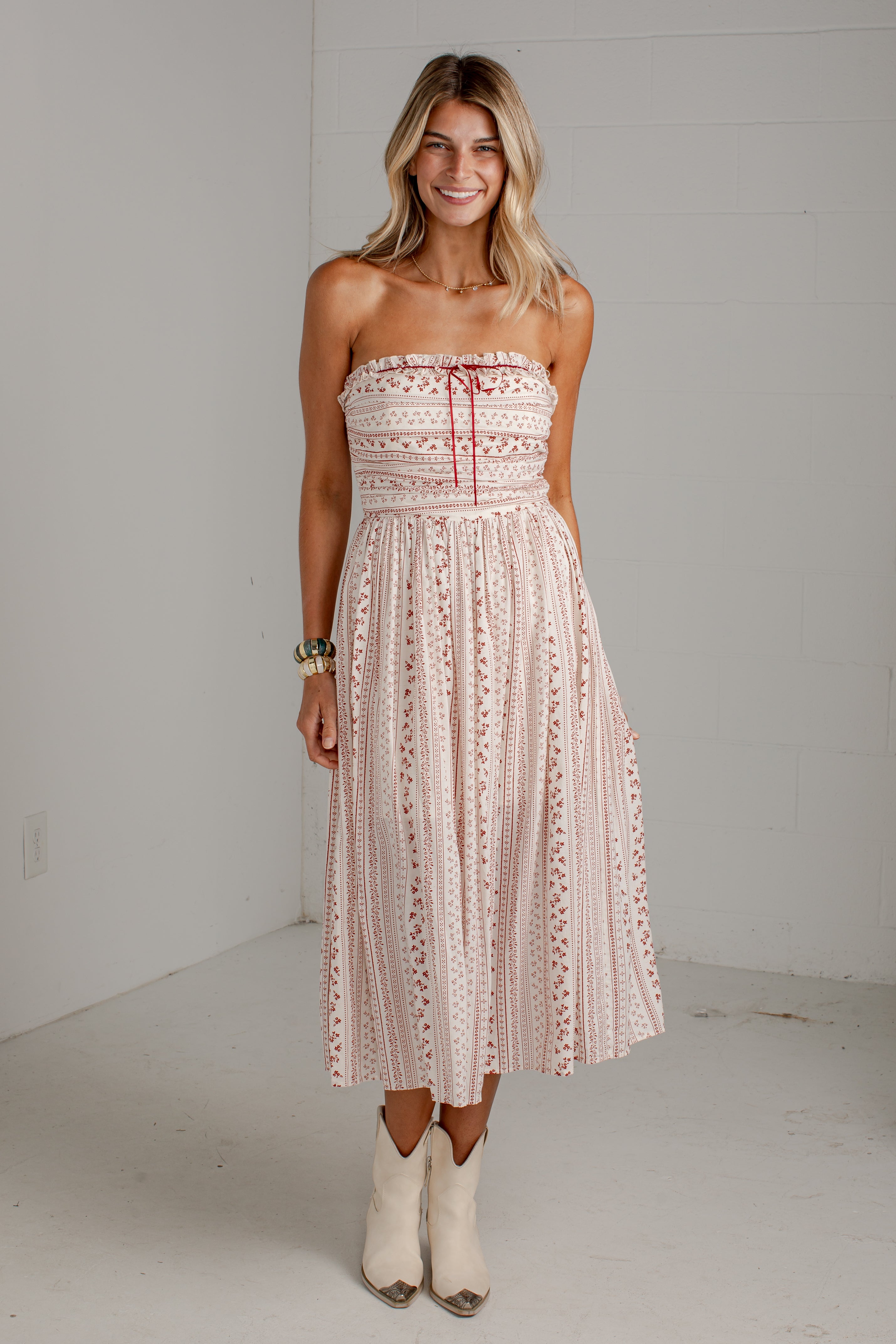 A woman modeling a strapless midi dress with a pink and white bohemian pattern, standing in a white studio setting.