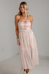A woman modeling a strapless midi dress with a light pink and white bohemian-style pattern and red tie details, standing against a white studio wall.