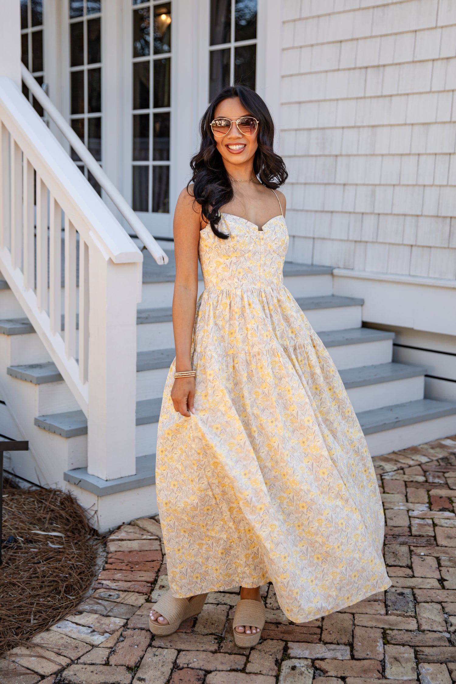 Woman in a yellow floral dress standing on a staircase outside a house.