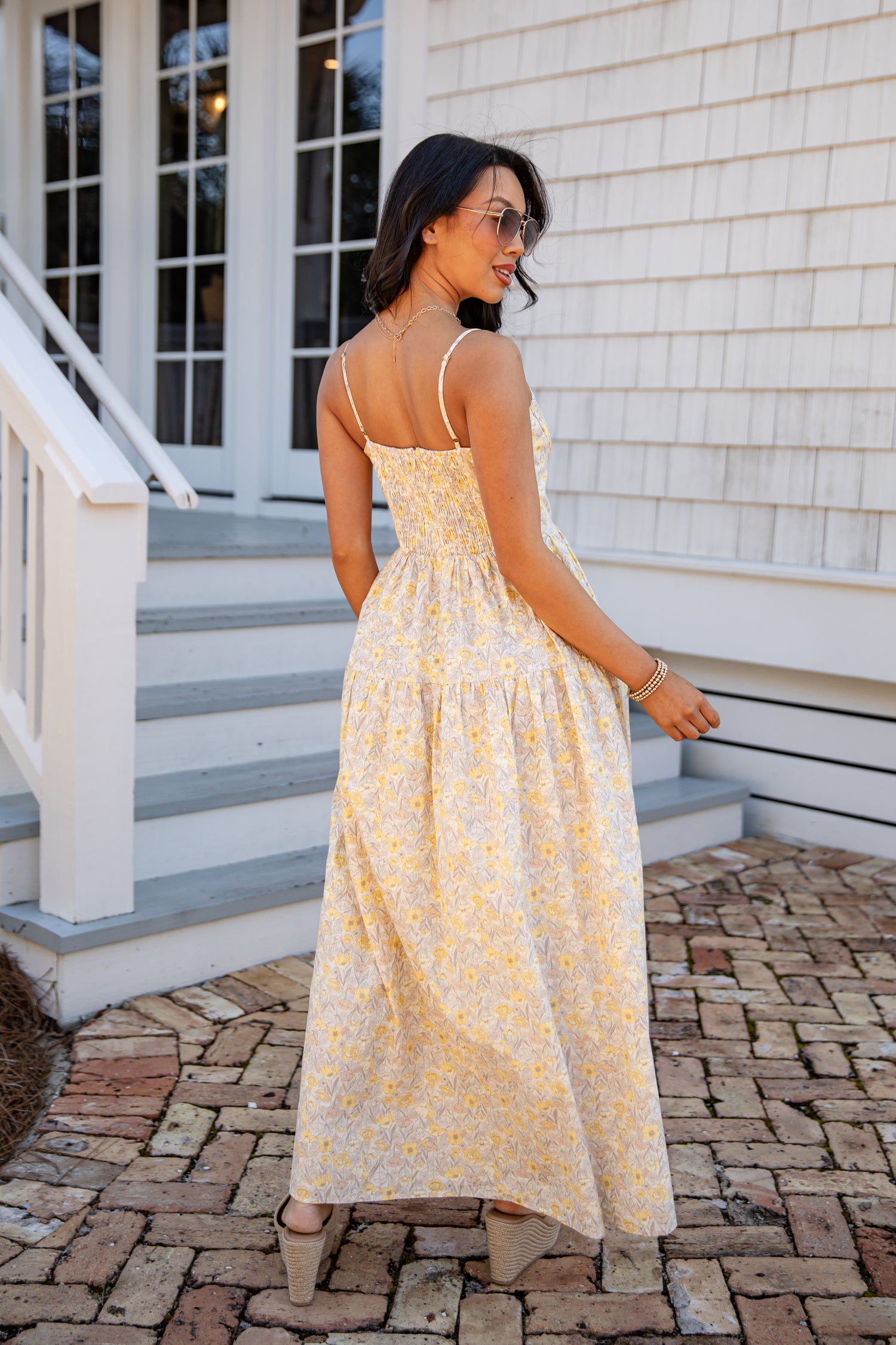 Woman in a yellow floral dress standing on a stone path in front of a house.