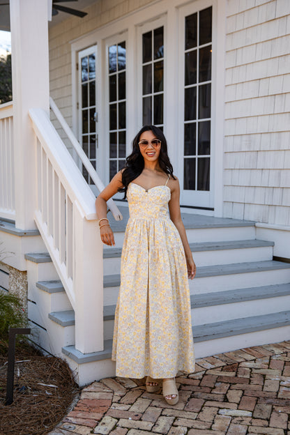 Woman in a yellow floral dress standing on a staircase outside a house.