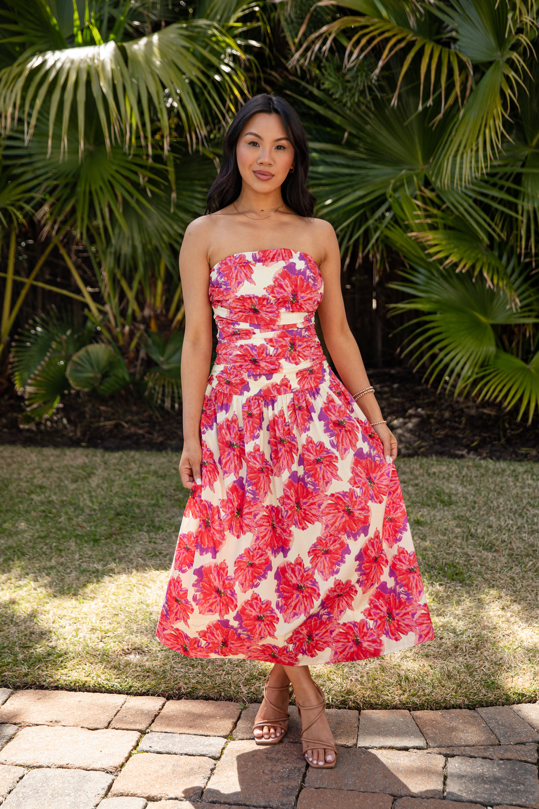 Woman wearing a strapless floral dress standing in front of tropical plants.