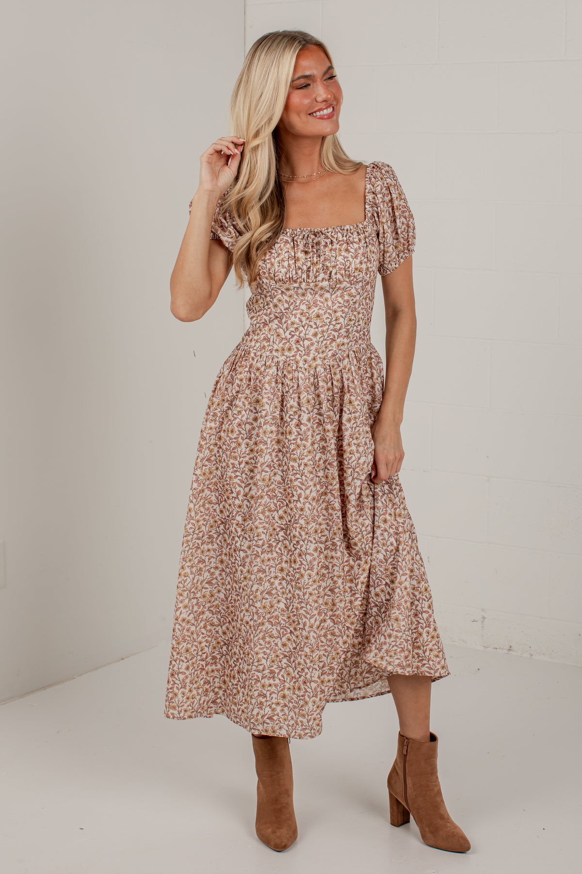 A woman modeling a short puff-sleeve midi dress with a brown and beige floral print, paired with brown suede ankle boots, set against a plain white studio background.