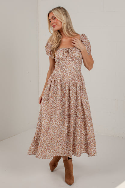 A woman modeling a midi-length puff-sleeve dress with a small beige and brown floral print, paired with brown ankle boots, set against a plain white studio background.