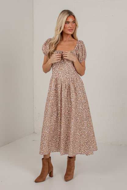 A woman modeling a midi-length puff-sleeve dress with a small-scale floral print in beige, brown, and muted pink tones, paired with brown suede ankle boots, set against a plain white studio background.