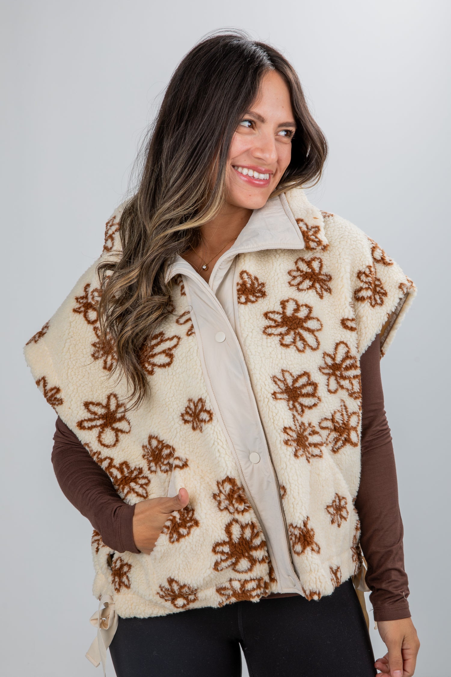 Woman wearing a cream-colored vest with brown floral patterns on a plain background
