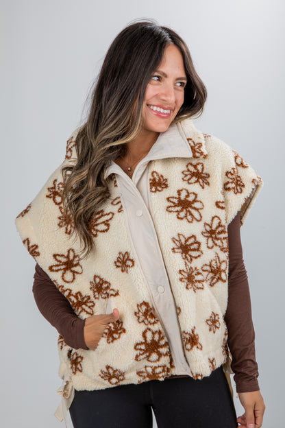 Woman wearing a cream-colored vest with brown floral patterns on a plain background