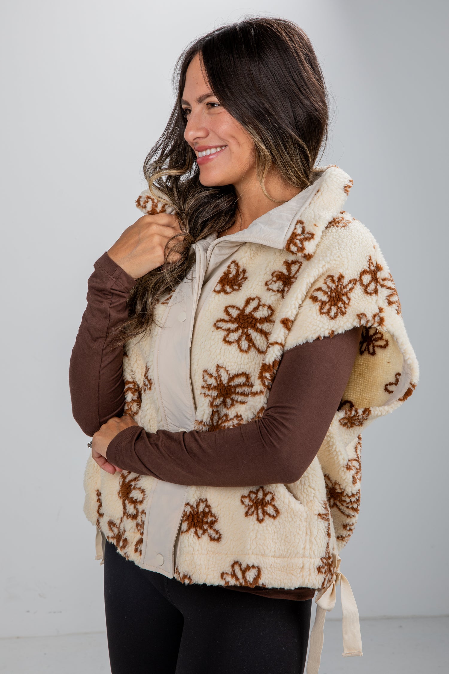 Woman wearing a beige floral-patterned poncho over a brown long-sleeve shirt against a white background