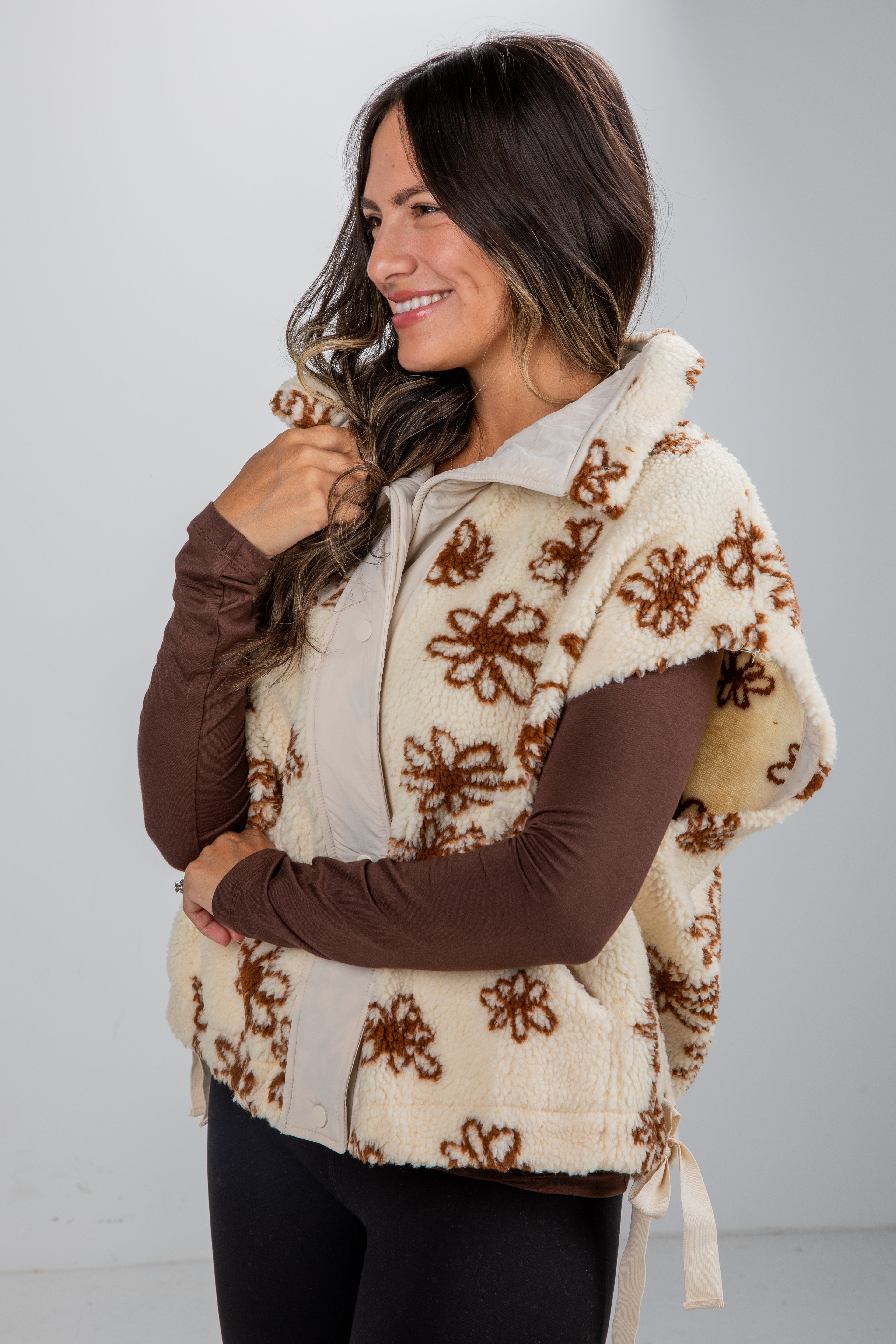 Woman wearing a beige floral-patterned poncho over a brown long-sleeve shirt against a white background