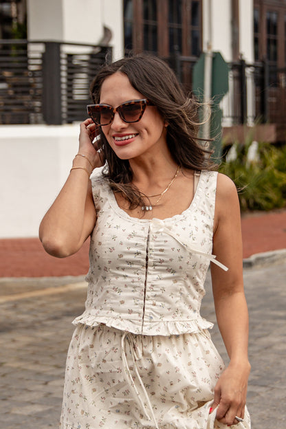 Woman in a white floral dress talking on a phone outdoors.