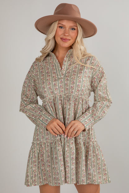Woman wearing a patterned dress and brown hat against a plain background