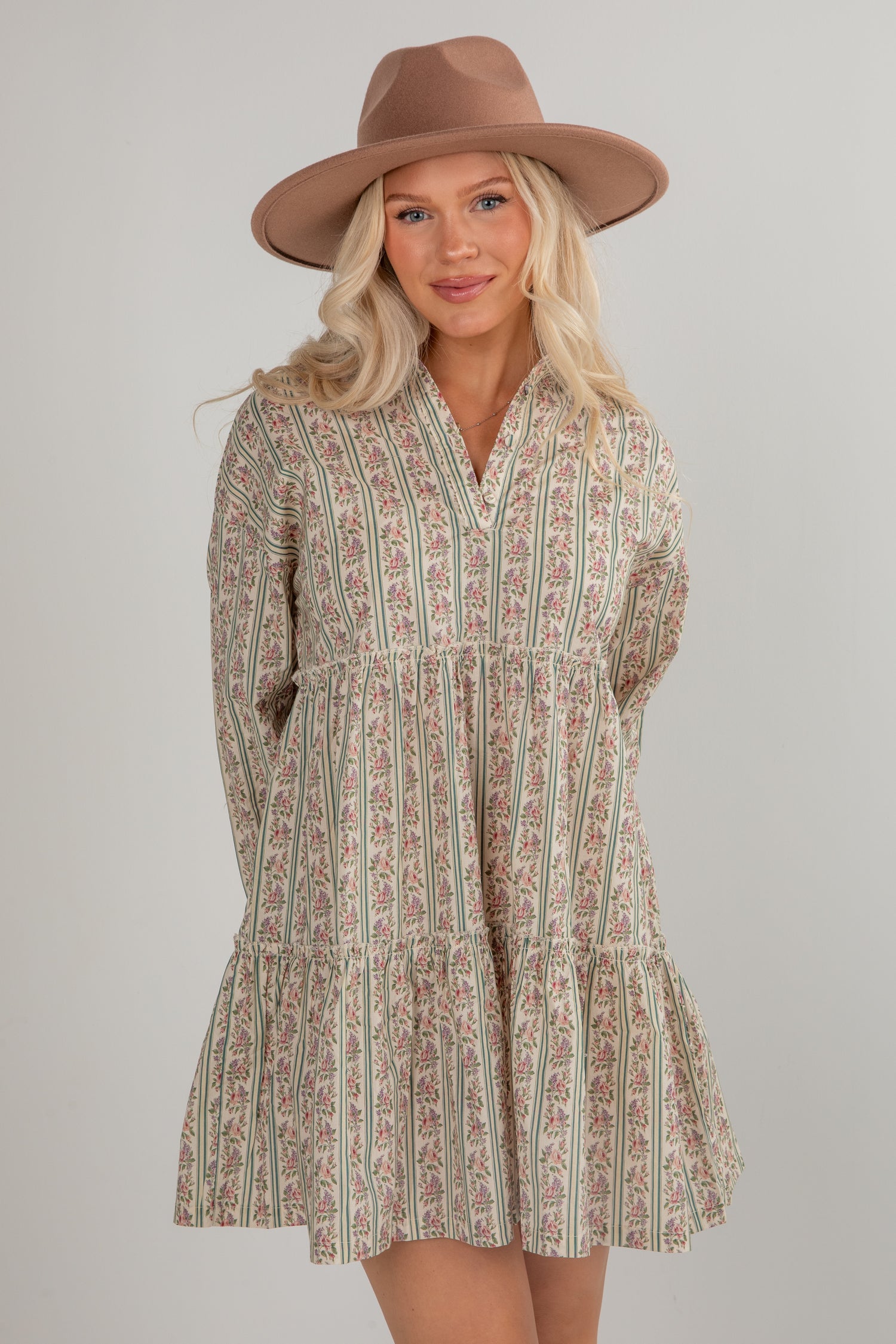 Woman wearing a patterned dress and brown hat on a plain background