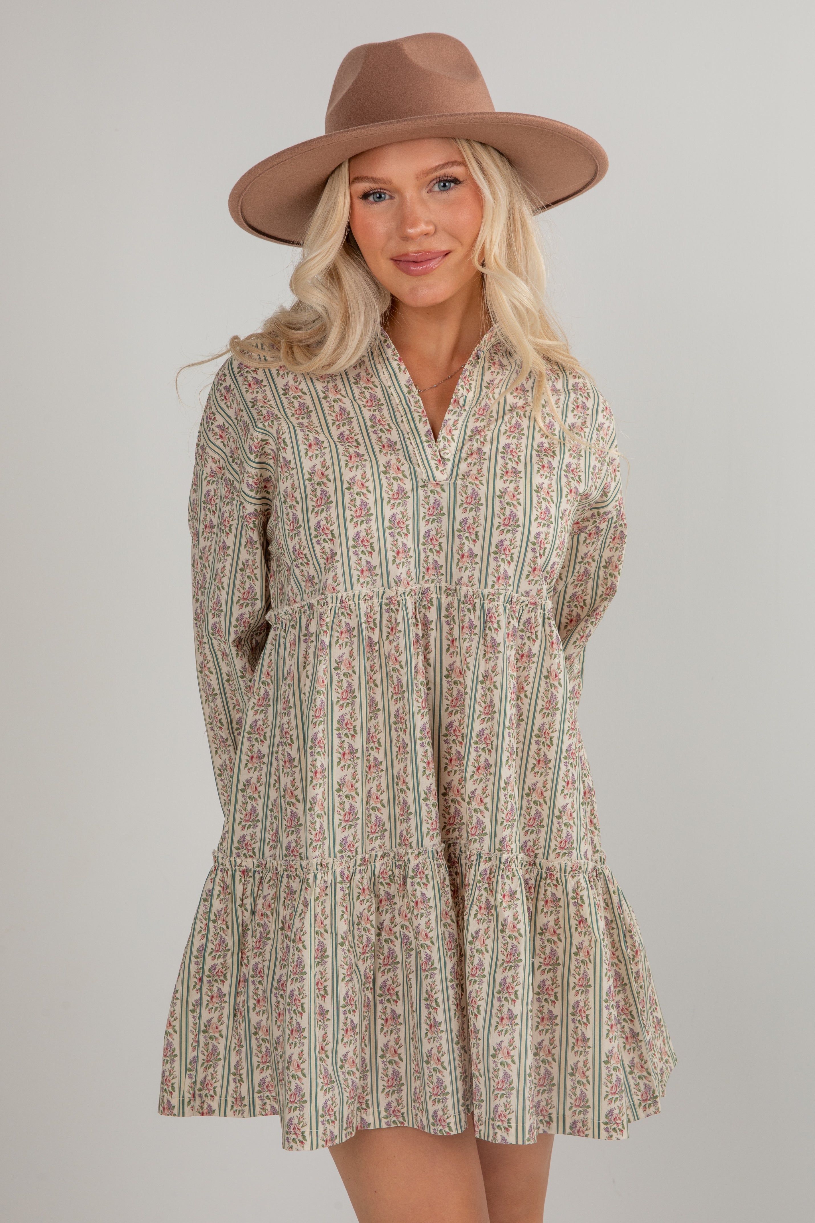 Woman wearing a patterned dress and brown hat on a plain background