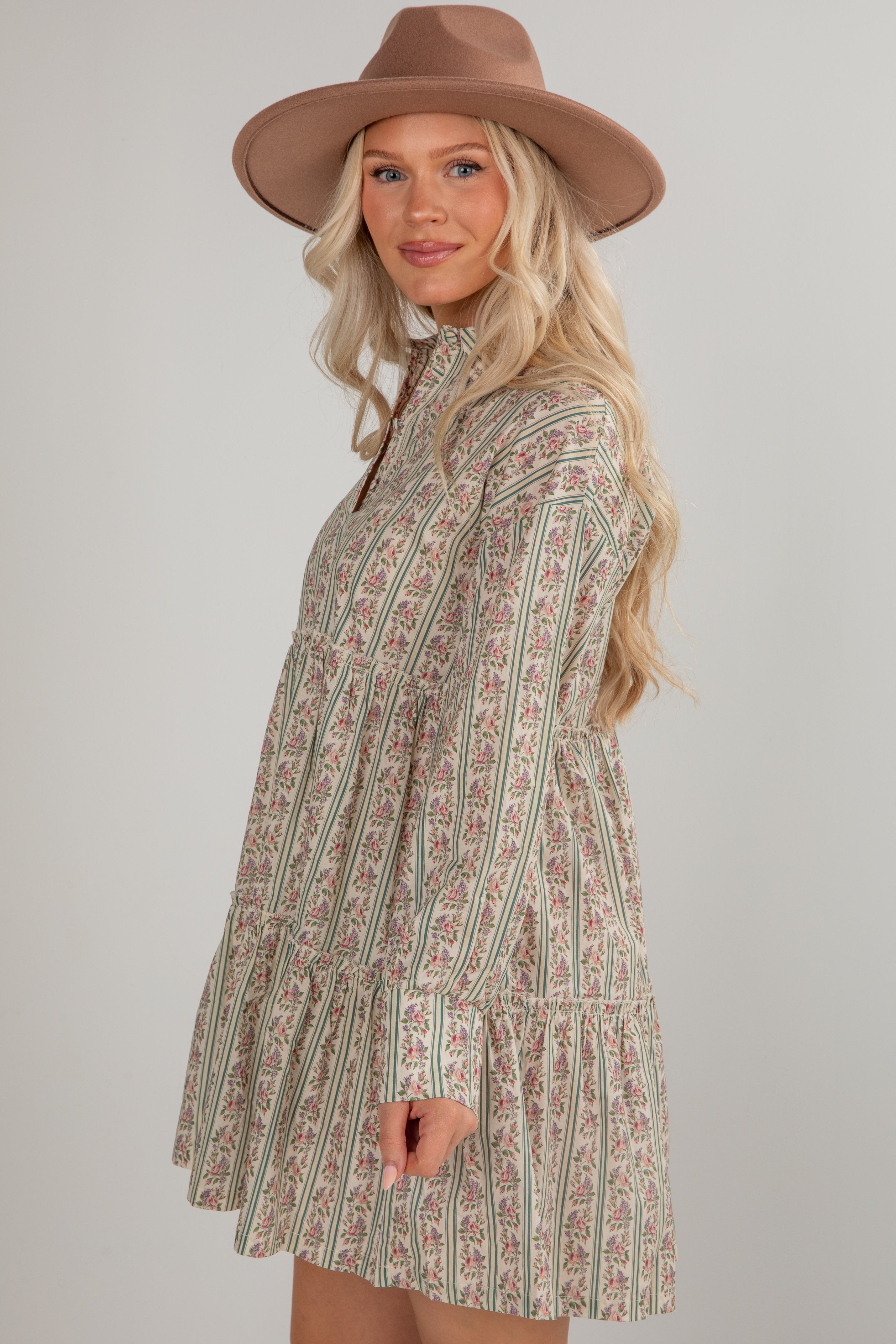 Woman wearing a patterned dress and brown hat against a plain background