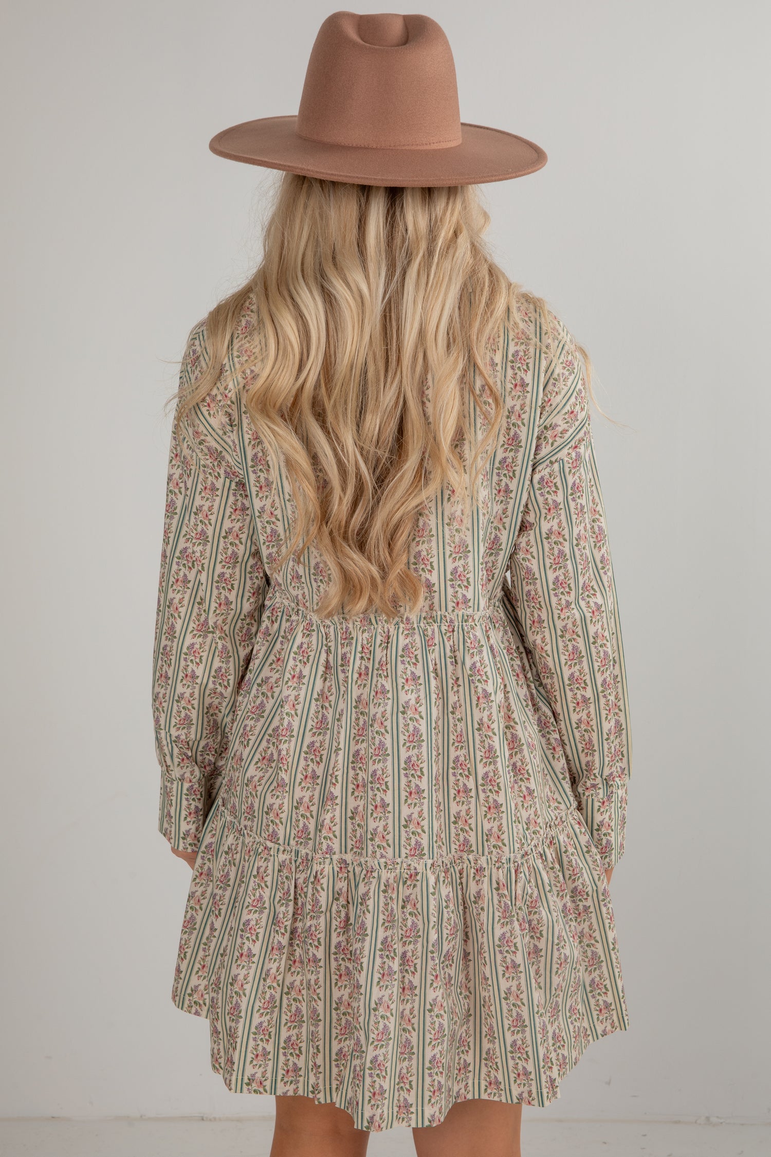 Person wearing a patterned dress and brown hat against a plain background