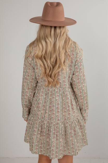 Person wearing a patterned dress and brown hat against a plain background