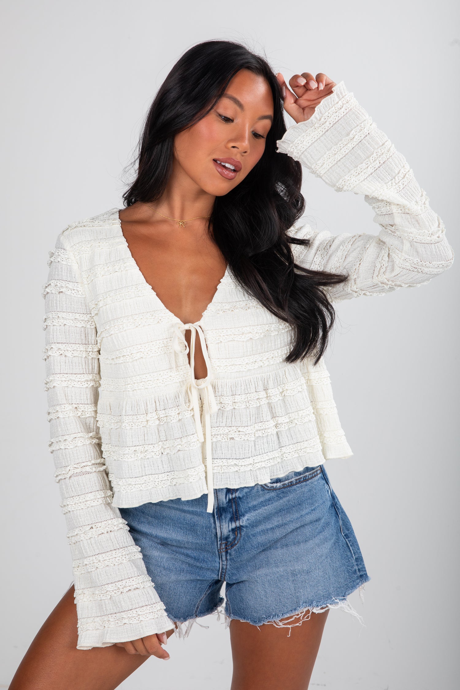 Woman wearing a white textured top and denim shorts on a plain background