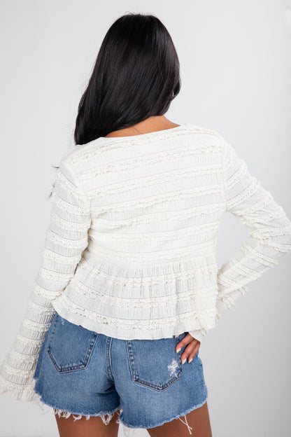 Person wearing a white textured jacket and denim shorts on a plain background