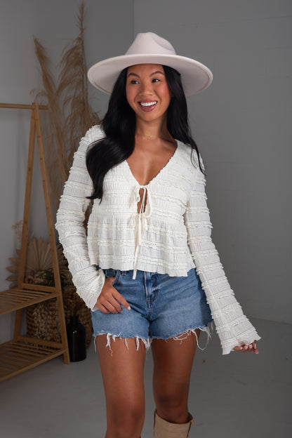 Woman wearing a white lace top and denim shorts with a white hat indoors.