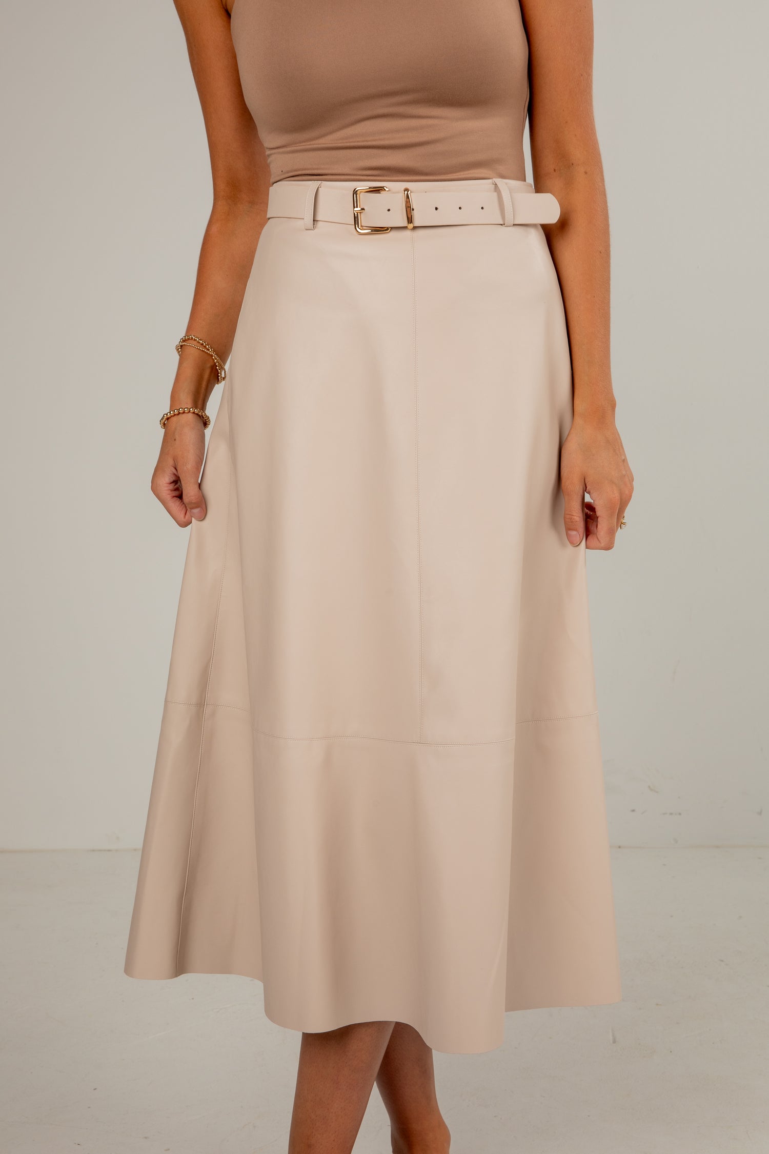 Person wearing a beige skirt with a belt on a plain background