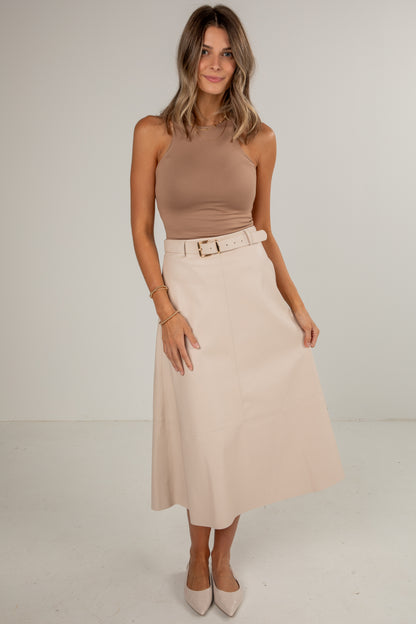 Woman wearing a beige sleeveless top and skirt with a belt on a plain background