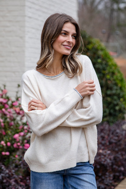 Woman wearing a cream sweater standing outdoors with flowers and a building in the background