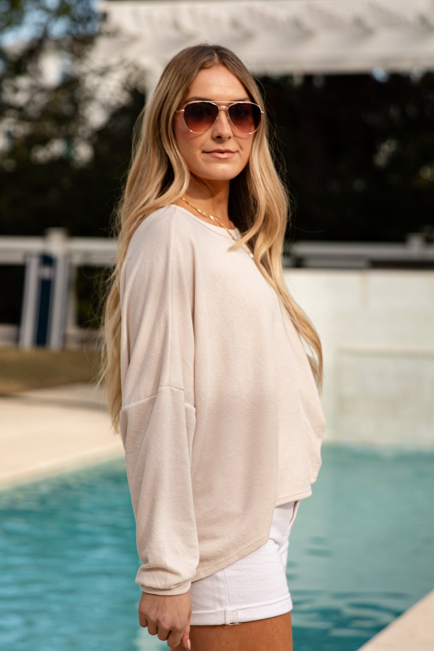 Woman wearing sunglasses and a beige top by a pool