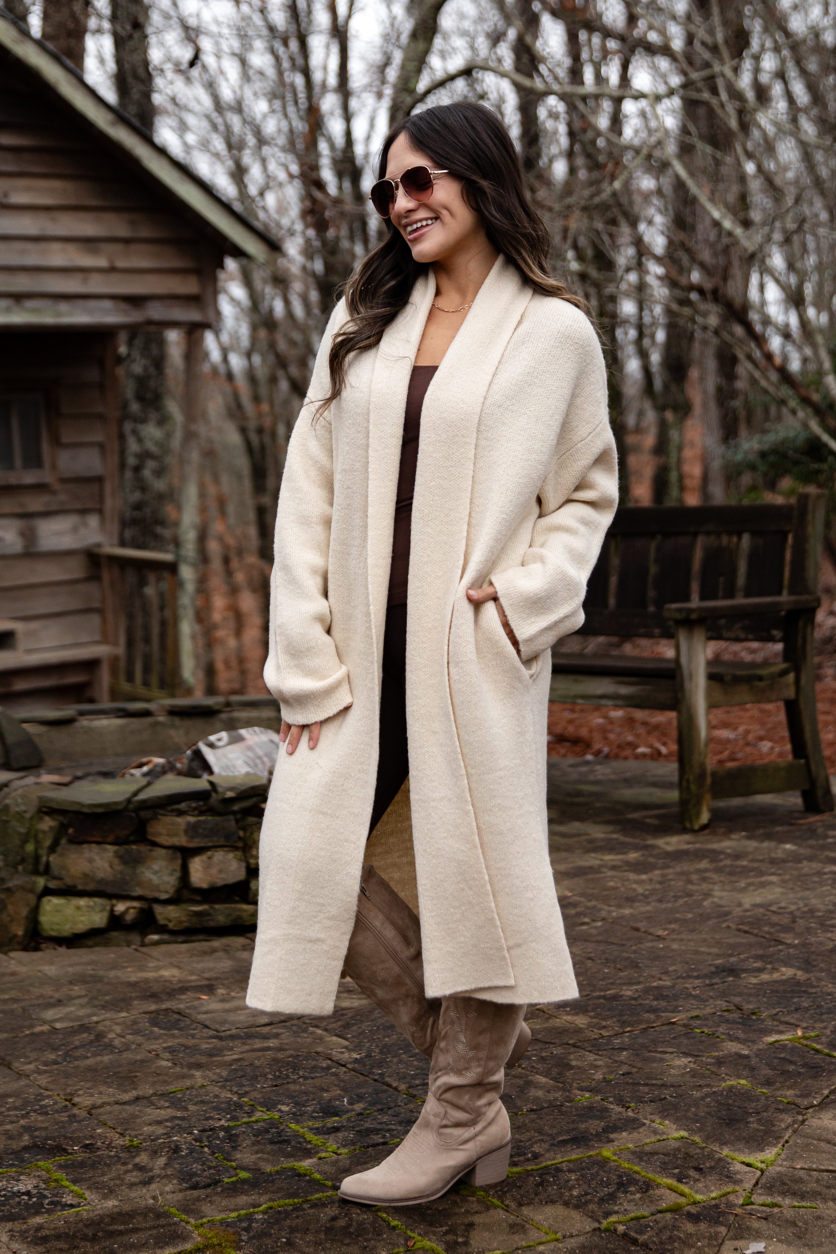 Woman wearing a long cream coat in a rustic outdoor setting
