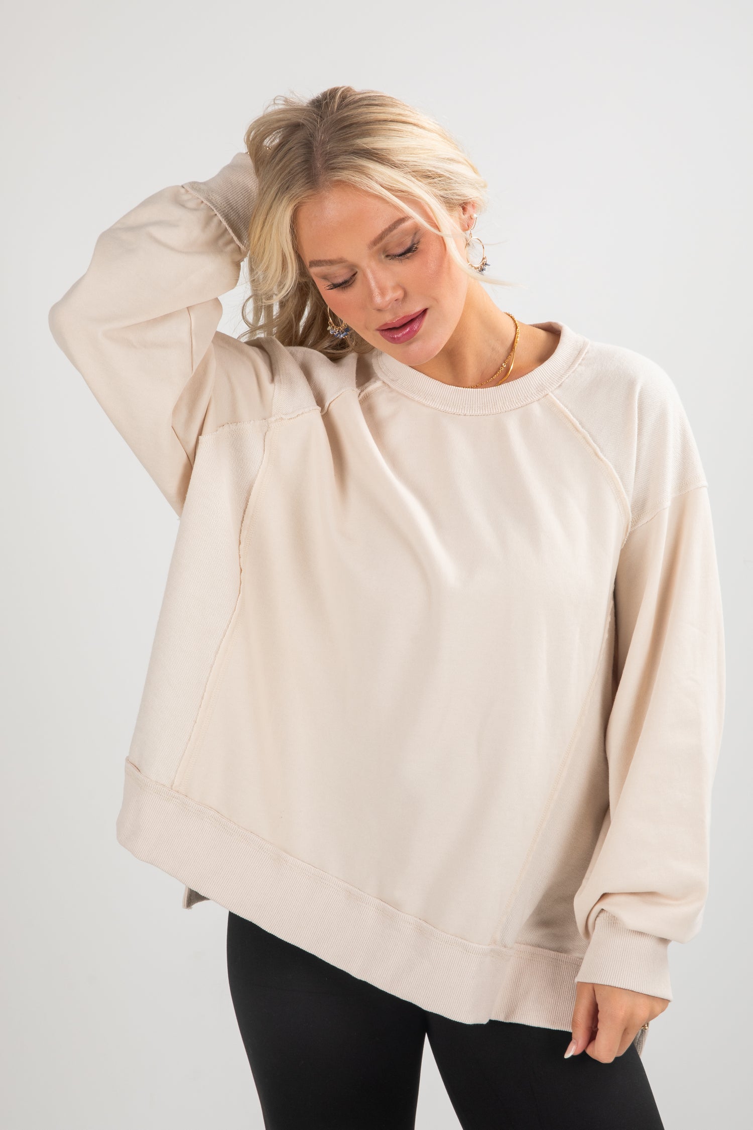 Woman wearing a beige oversized sweatshirt against a white background
