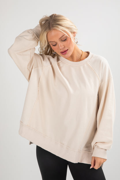 Woman wearing a beige oversized sweatshirt against a white background