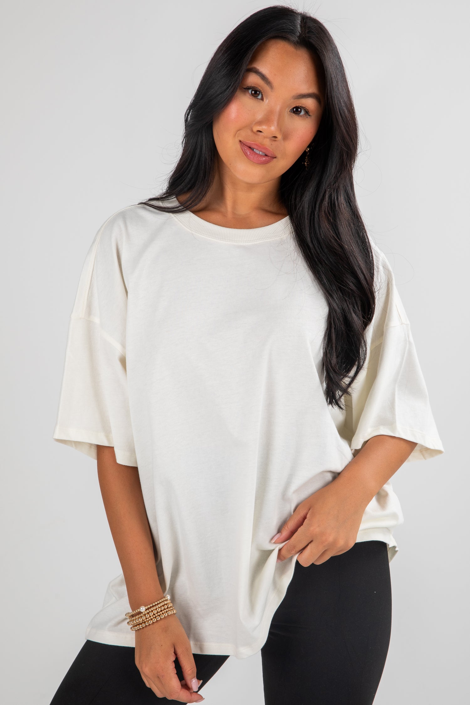 Woman wearing a white oversized t-shirt and black pants on a plain background