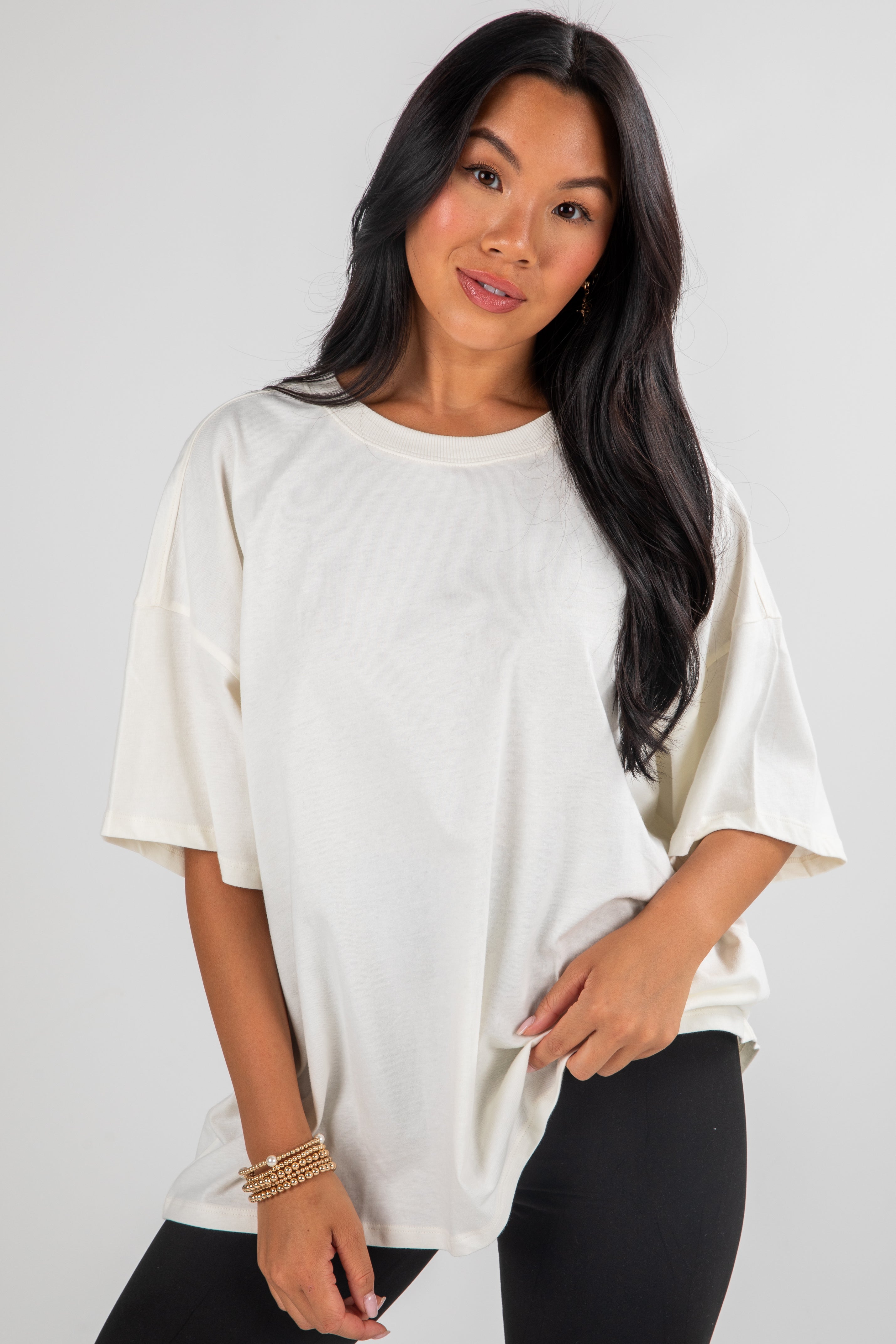 Woman wearing a white oversized t-shirt and black pants on a plain background