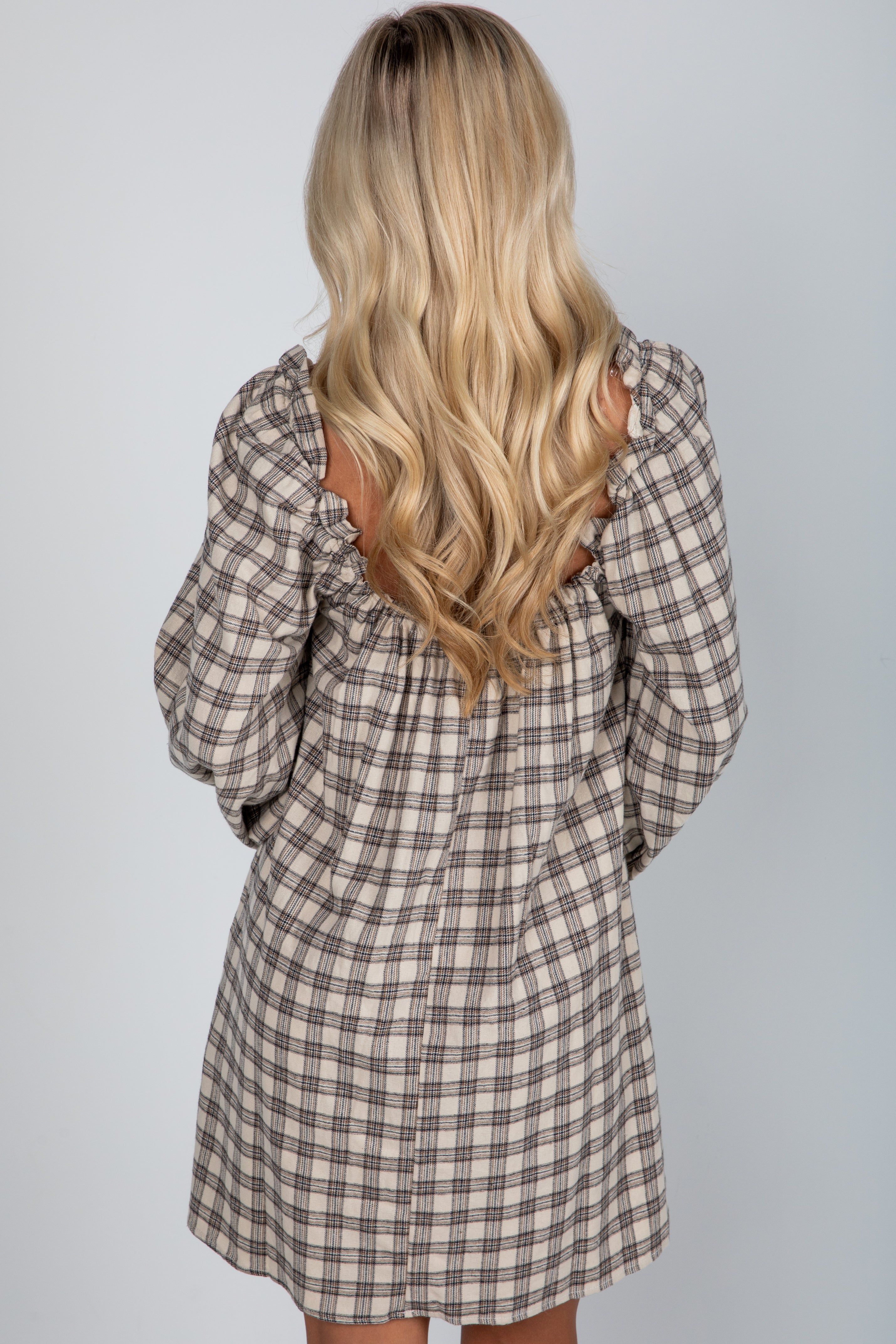 Person wearing a plaid dress with long blonde hair on a plain background