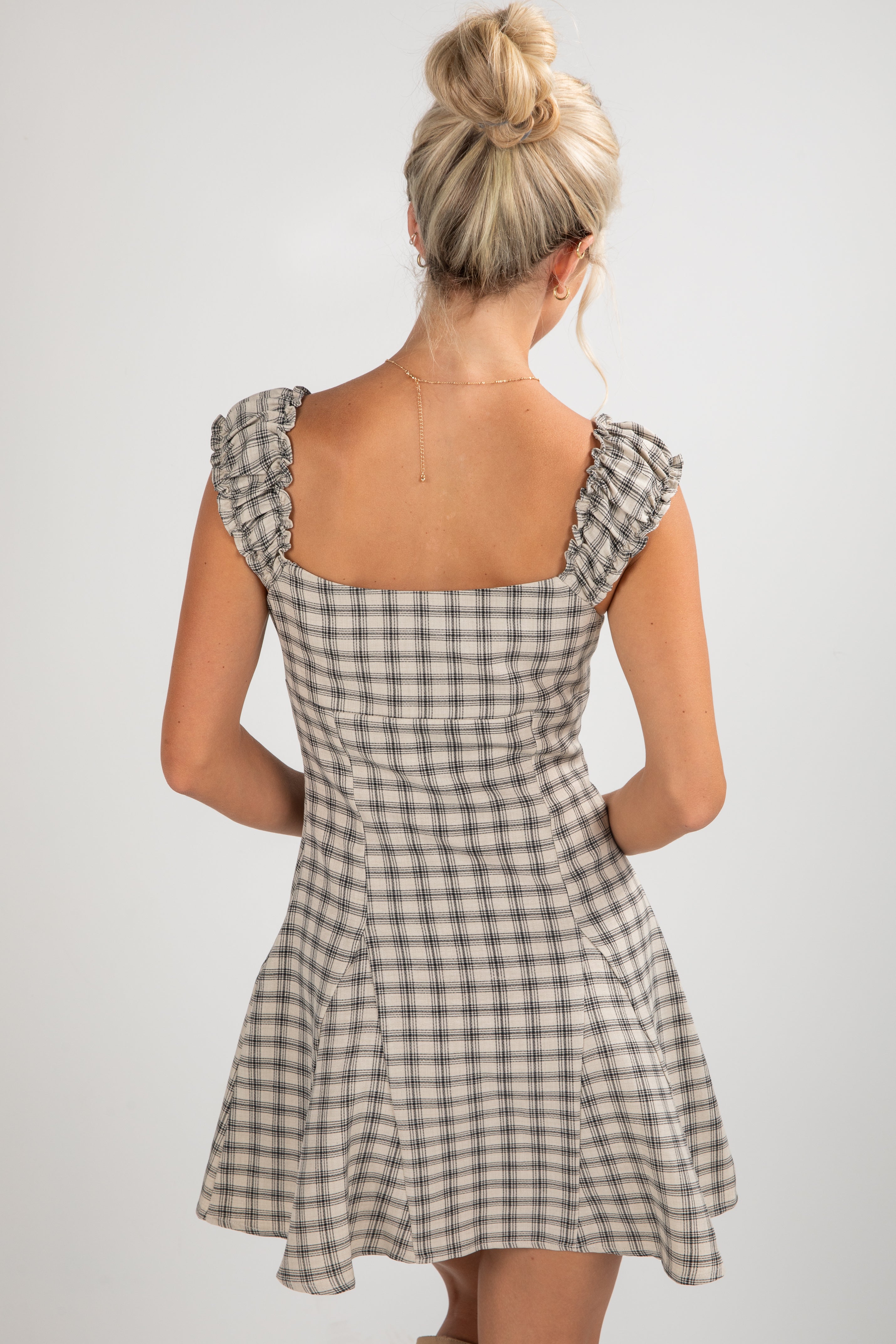 Woman wearing a checkered dress with ruffled shoulders on a plain background