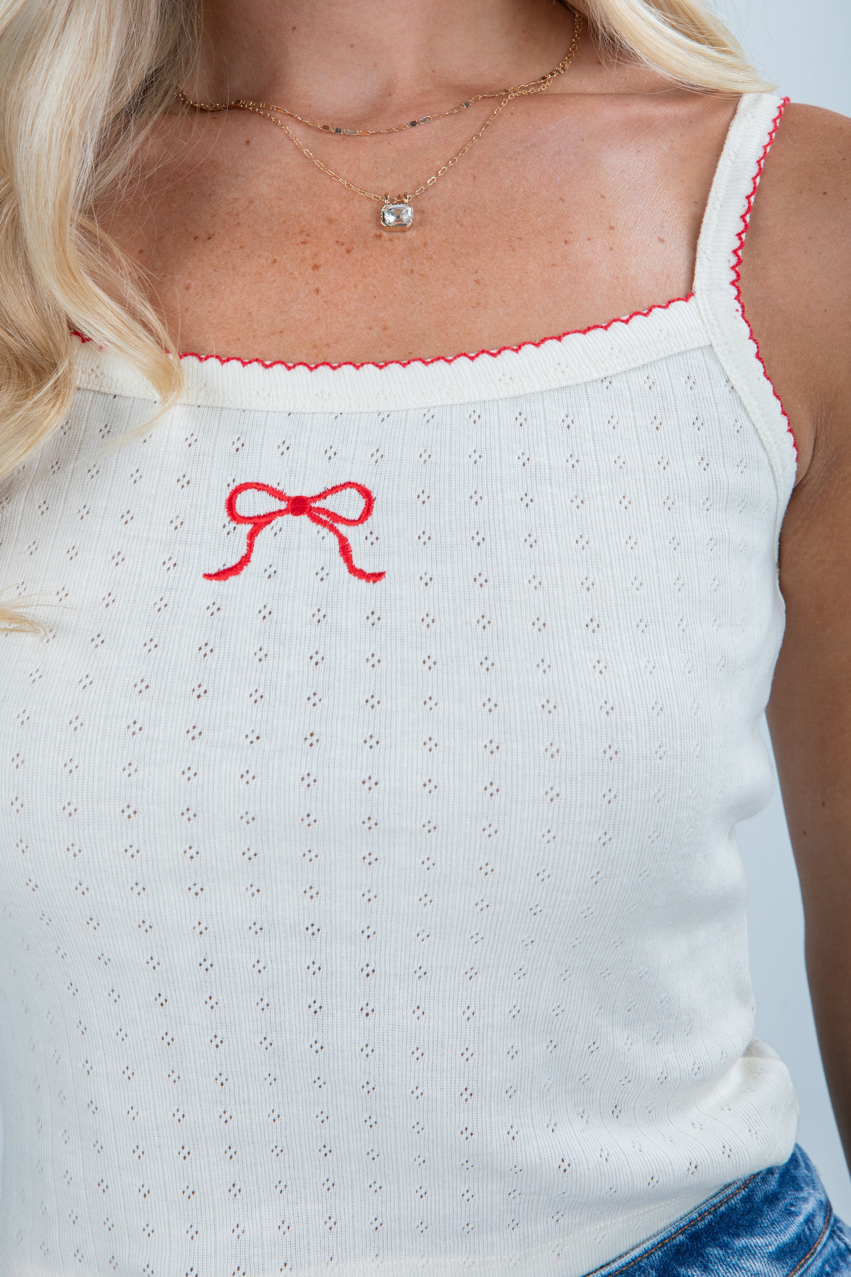 White tank top with red bow detail and blue jeans