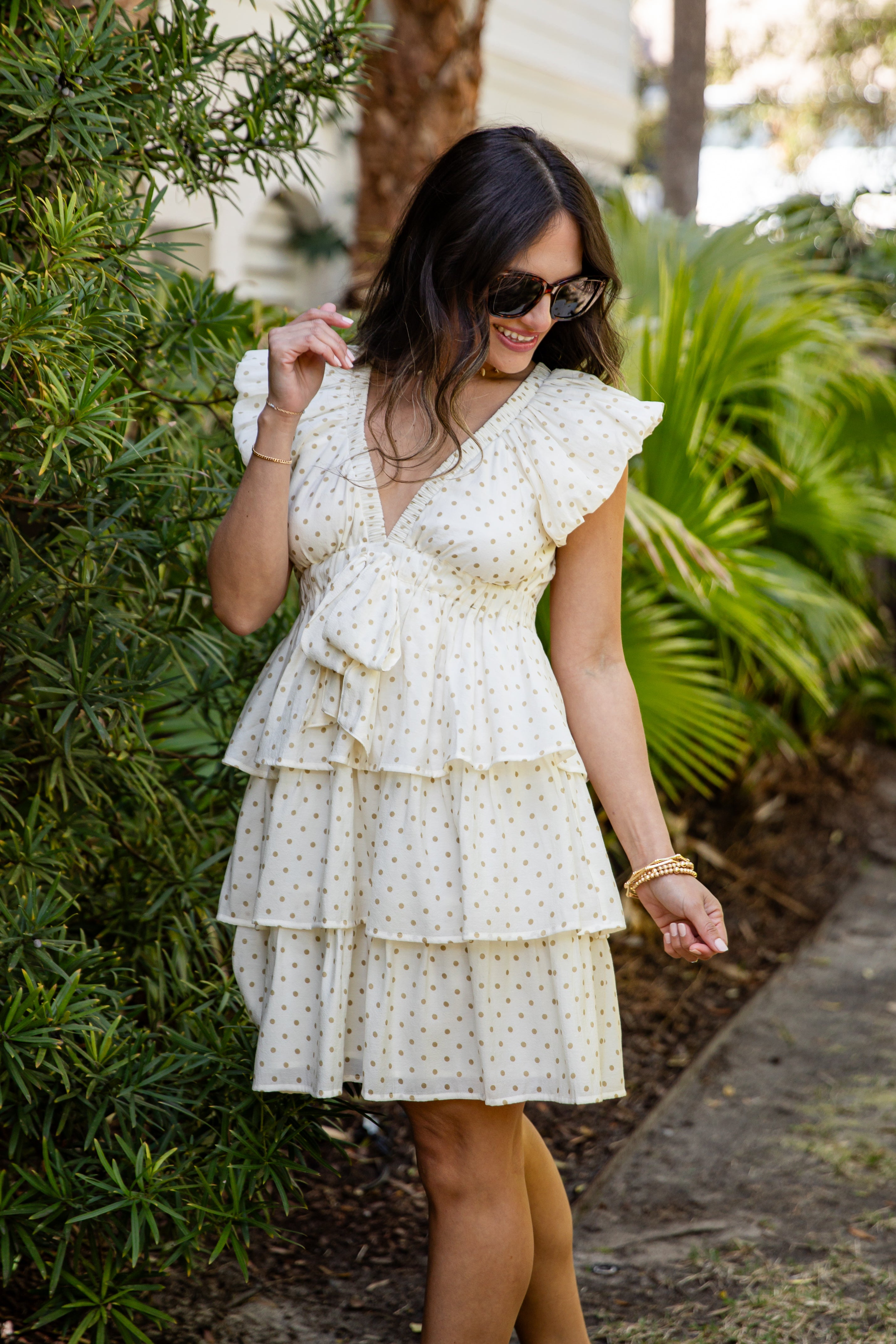Woman wearing a white polka dot dress standing outdoors with greenery in the background