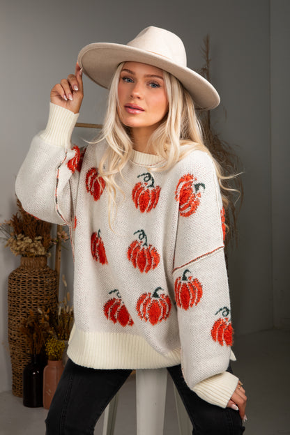Woman wearing a cream sweater with red pumpkin patterns and a beige hat indoors.