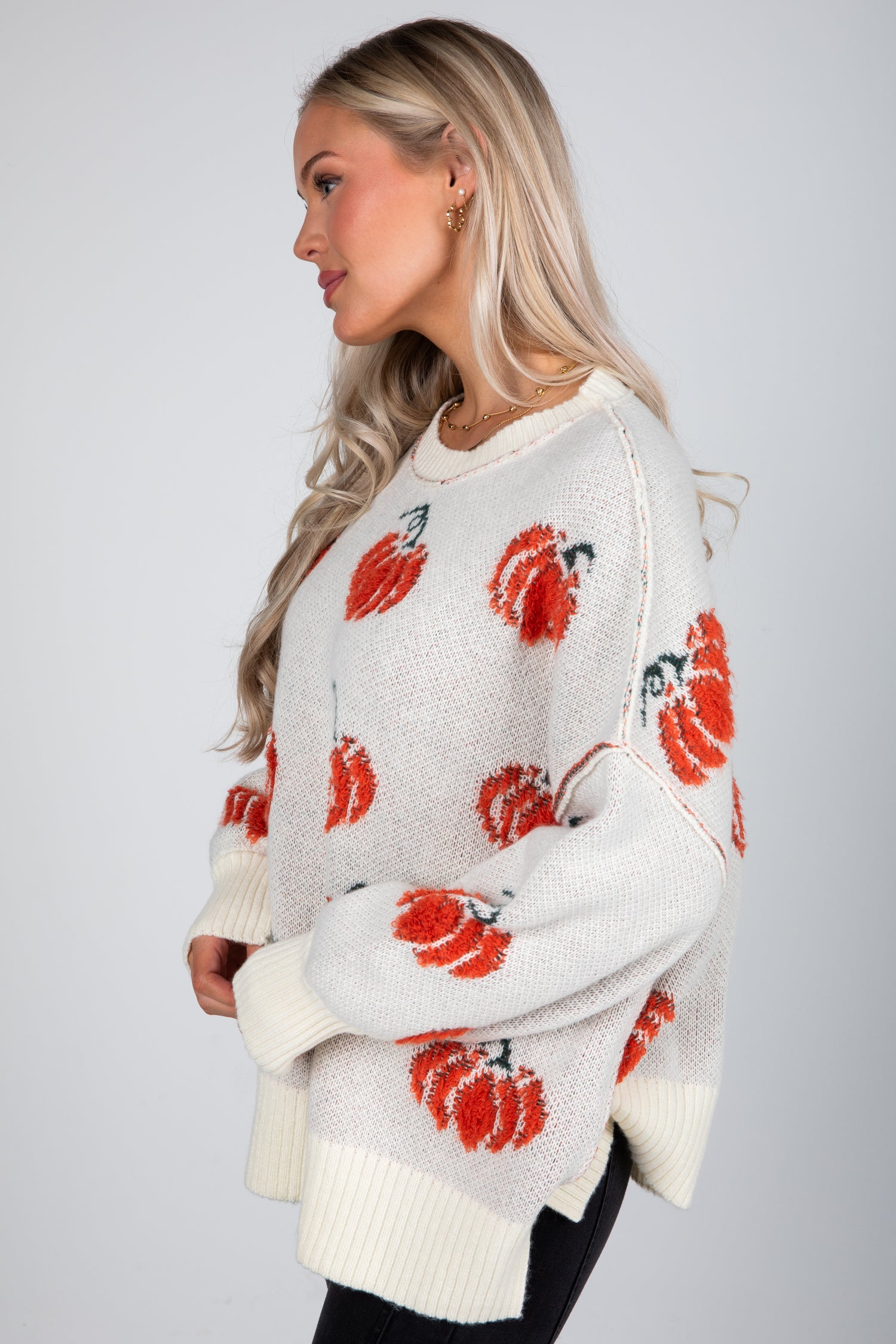 Woman wearing a white sweater with red floral patterns on a plain background
