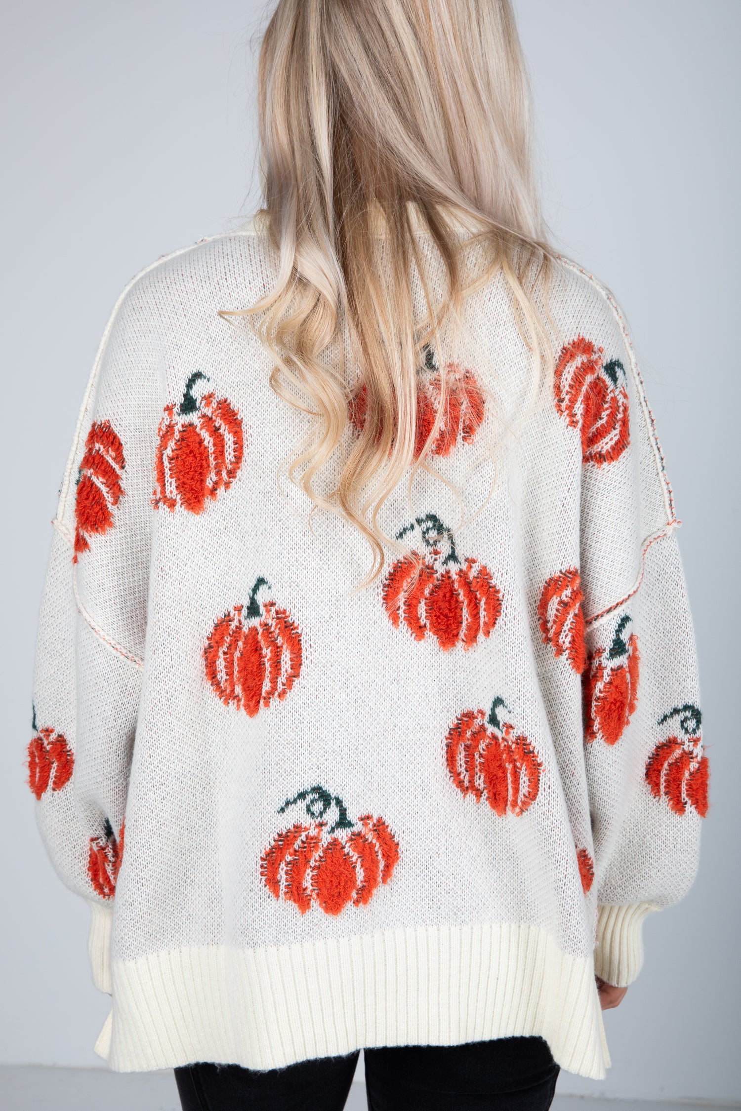 White sweater with red pumpkin patterns worn by a person with blonde hair.