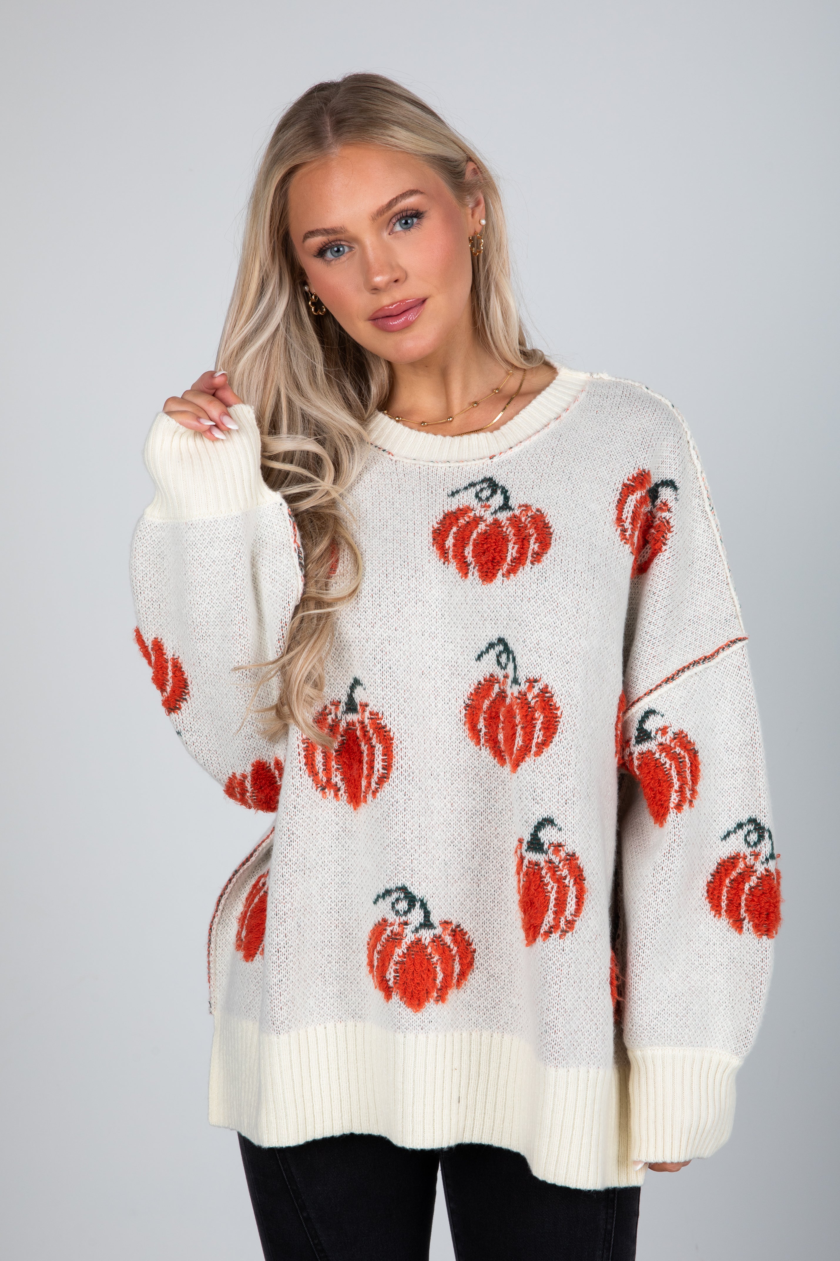 Woman wearing a white sweater with red pumpkin patterns on a gray background