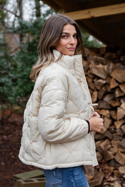 Woman wearing a white quilted jacket standing in front of stacked firewood.