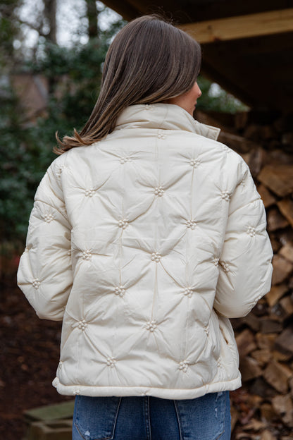 Person wearing a cream quilted jacket with a blurred natural background