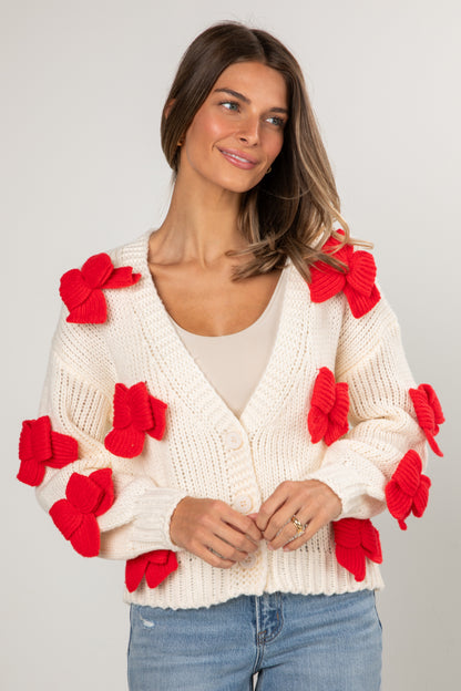 Woman wearing a white sweater with red floral attachments on a plain background