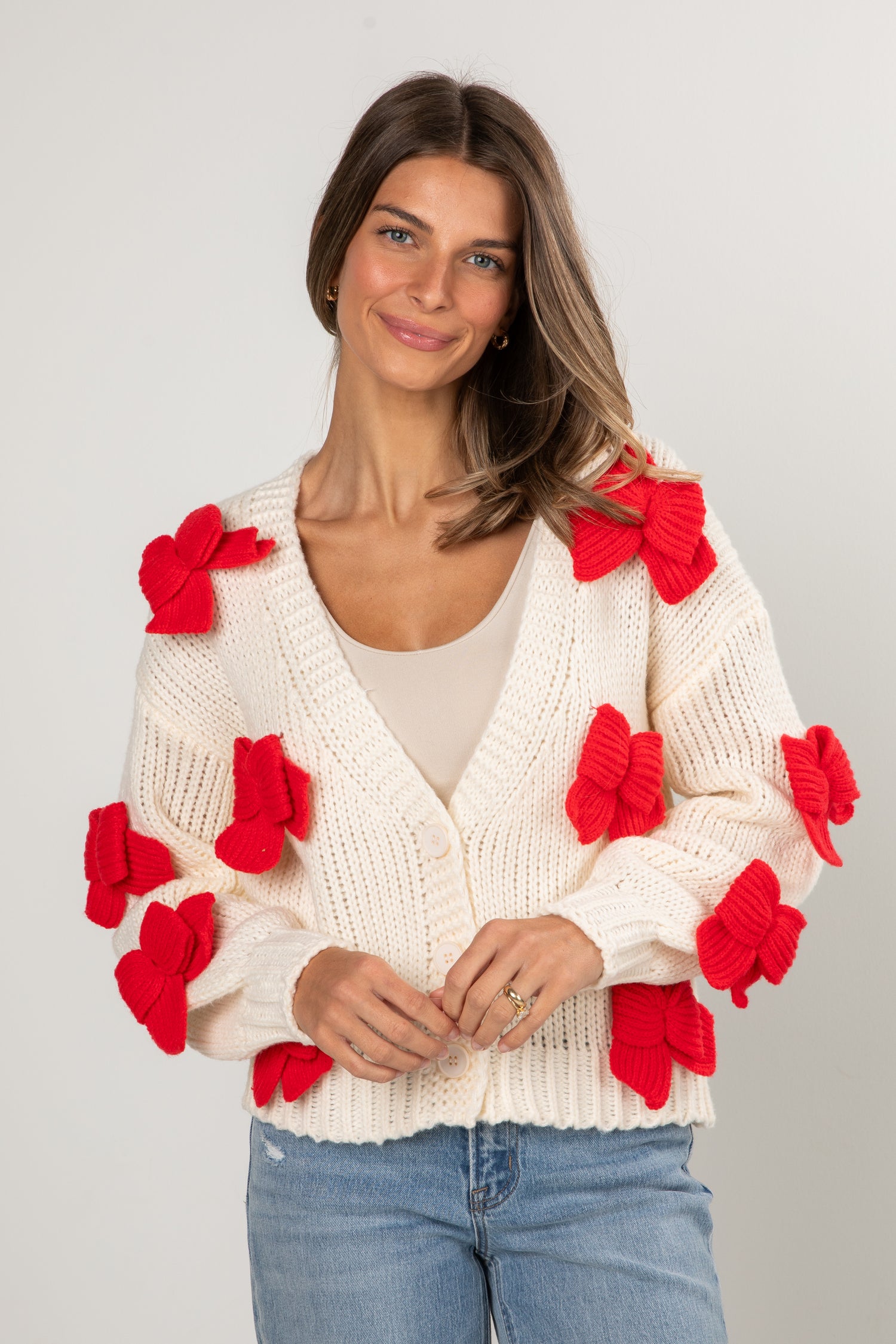 Woman wearing a white sweater with red floral attachments on a plain background