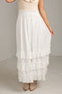 A white tiered maxi skirt with a smocked elastic waistband, shown on a model wearing beige ankle boots against a neutral studio background.